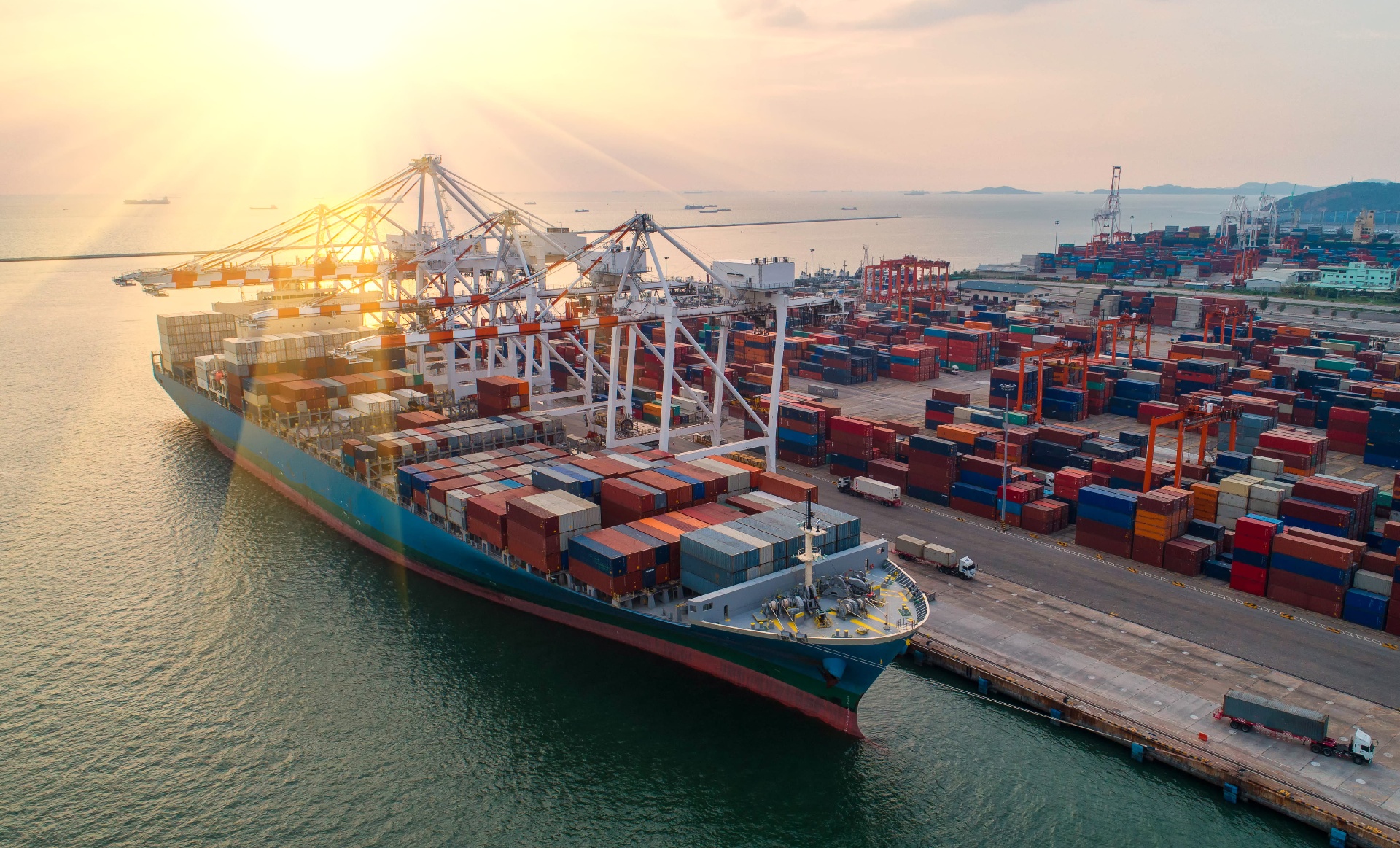 Port cranes loading a container ship at sunset